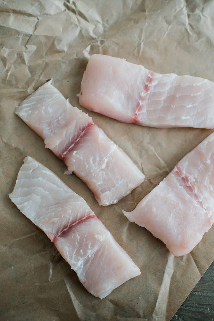Quatro pedaços de peixe cru pronto a cozinhar em papel pardo de talho