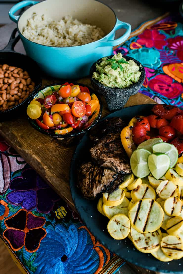 mesa de madeira coberta com ingredientes para montar tigelas de burrito - vegetais grelhados, pico de gallo, guacamole, frijoles de la olla e arroz verde chile eclosão