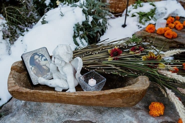 tigela de madeira com um quadro emoldurado, uma vela de chá, uma pequena estátua de querubim e calêndulas para celebrar o dia dos mortos.