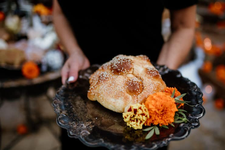 latina segurando um prato preto com dois elementos de dia de los muertos: pão especial e calêndulas para um dia de celebração dos mortos