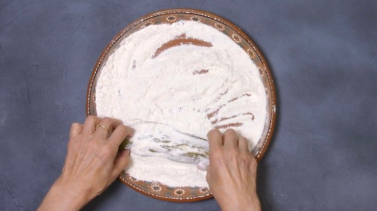 duas mãos cobrindo as pimentas em mistura de farinha