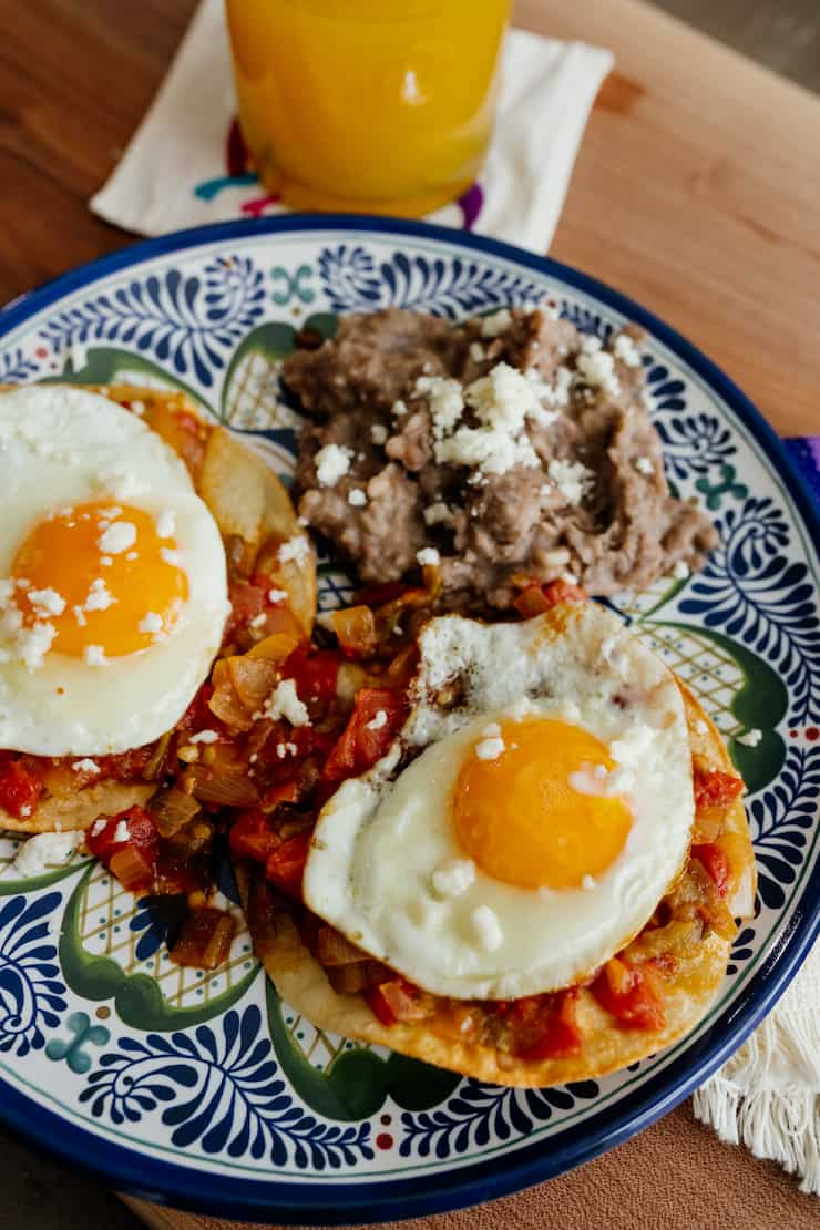 huevos rancheros em um prato azul e branco com feijão frito e dois ovos ao sol