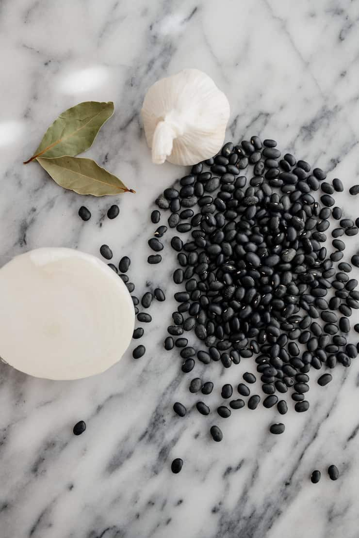 feijão preto, cebola, alho e folha de louro sobre superfície de mármore cinzento e branco