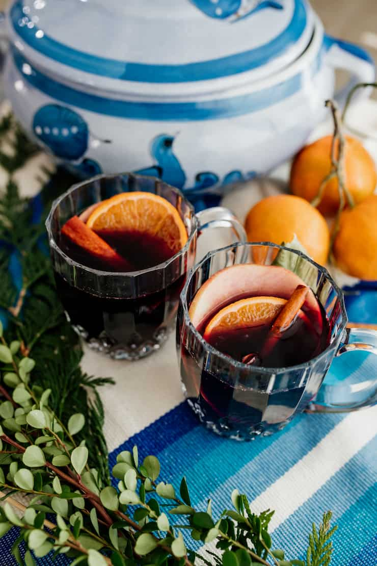 duas canecas de vidro de vinho temperado com pau de canela e guarnições em fatia de laranja numa paisagem de mesa azul e branca