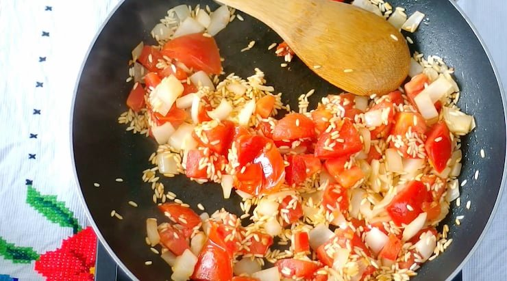 arroz, cebola e tomate cozinhando em uma frigideira com uma colher de pau