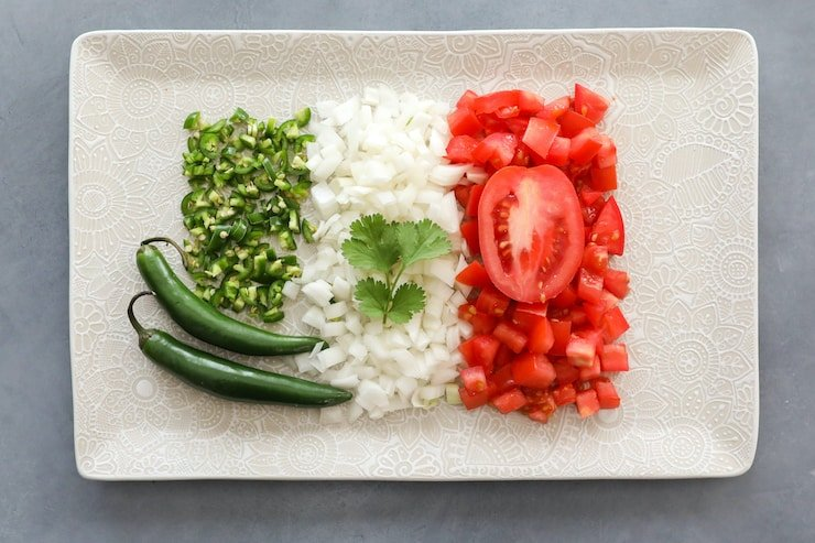 pimentas, cebolas e tomates dispostos de forma a parecerem a bandeira mexicana num prato rectangular branco com um raminho de coentro fresco