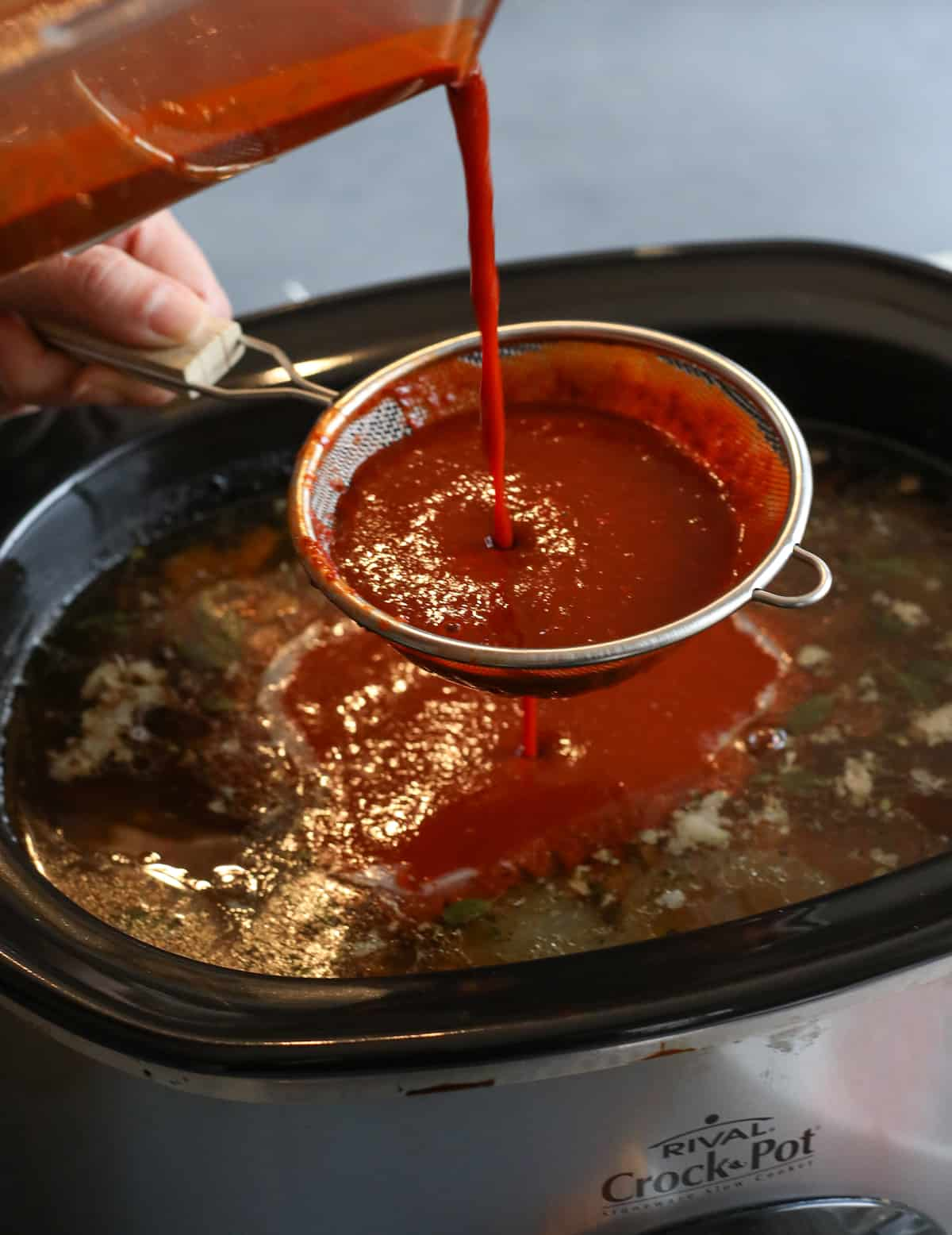 molho de chile vermelho caseiro, deitado à mão, através de um coador, no pote com a bétria