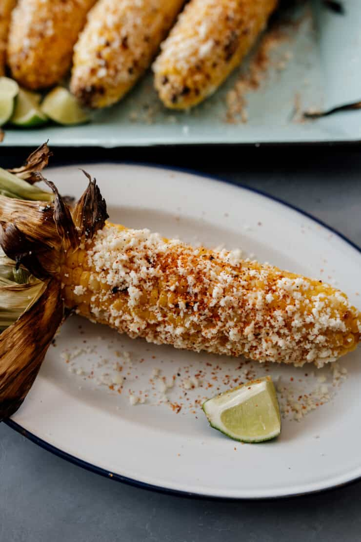 uma espiga de milho de rua mexicana num prato branco oblongo com uma cunha de lima