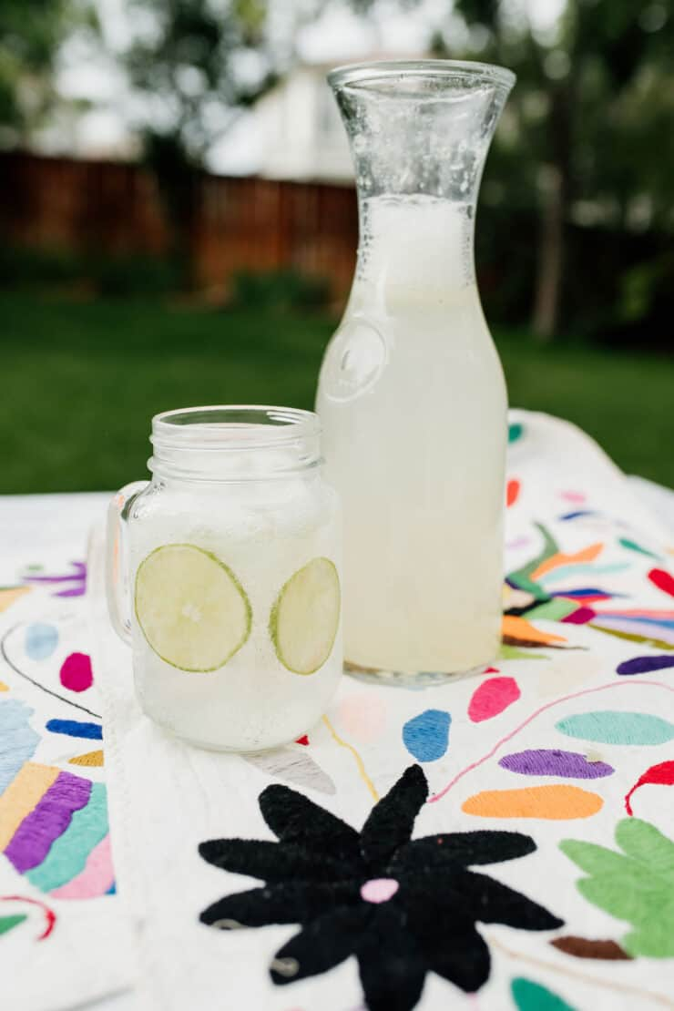 jarro de pedreiro com cabo cheio de limonada cintilante e fatias redondas de lima numa manta de piquenique junto a um jarro de limonada