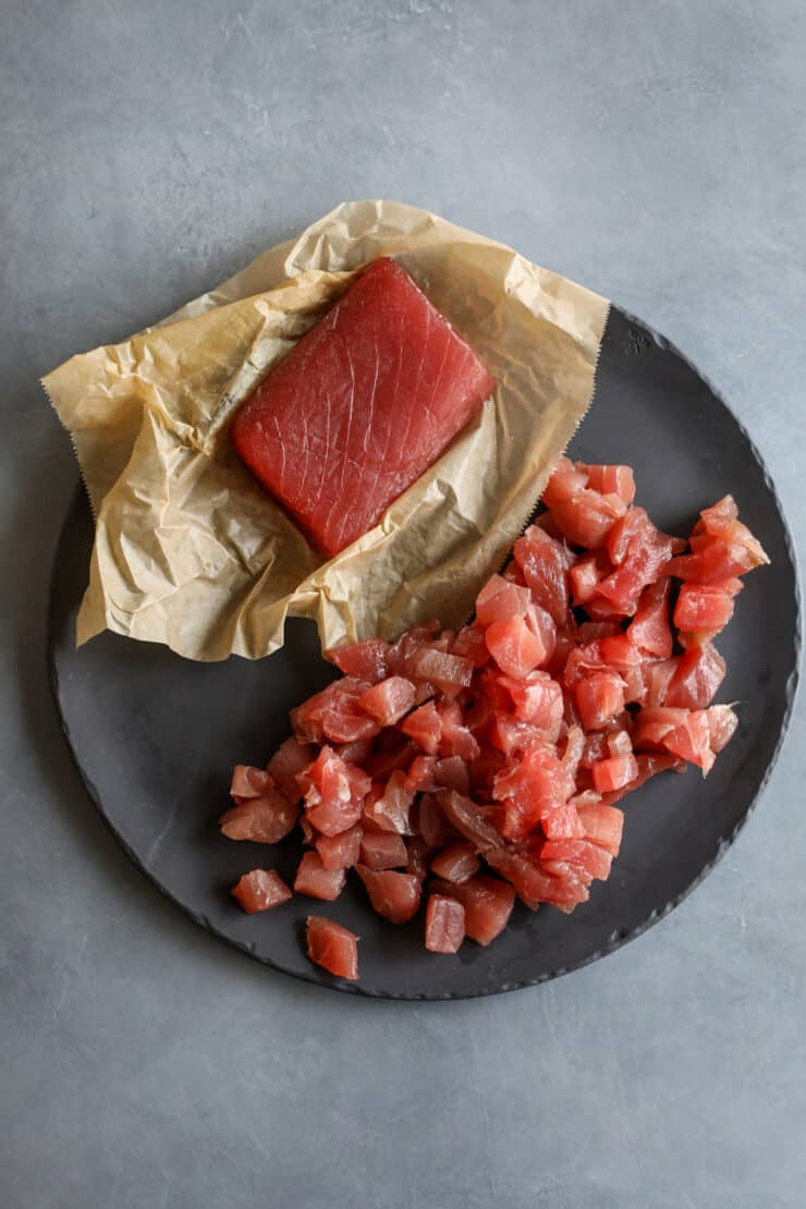 pedaço de atum cru num pedaço de pergaminho ao lado de cubos de atum num prato de ardósia