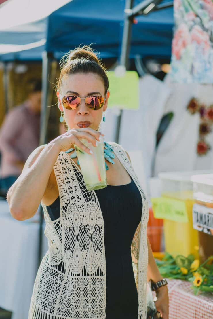 A blogueira da latina Yvette Marquez bebendo um copo de agua de pepino no mercado do fazendeiro