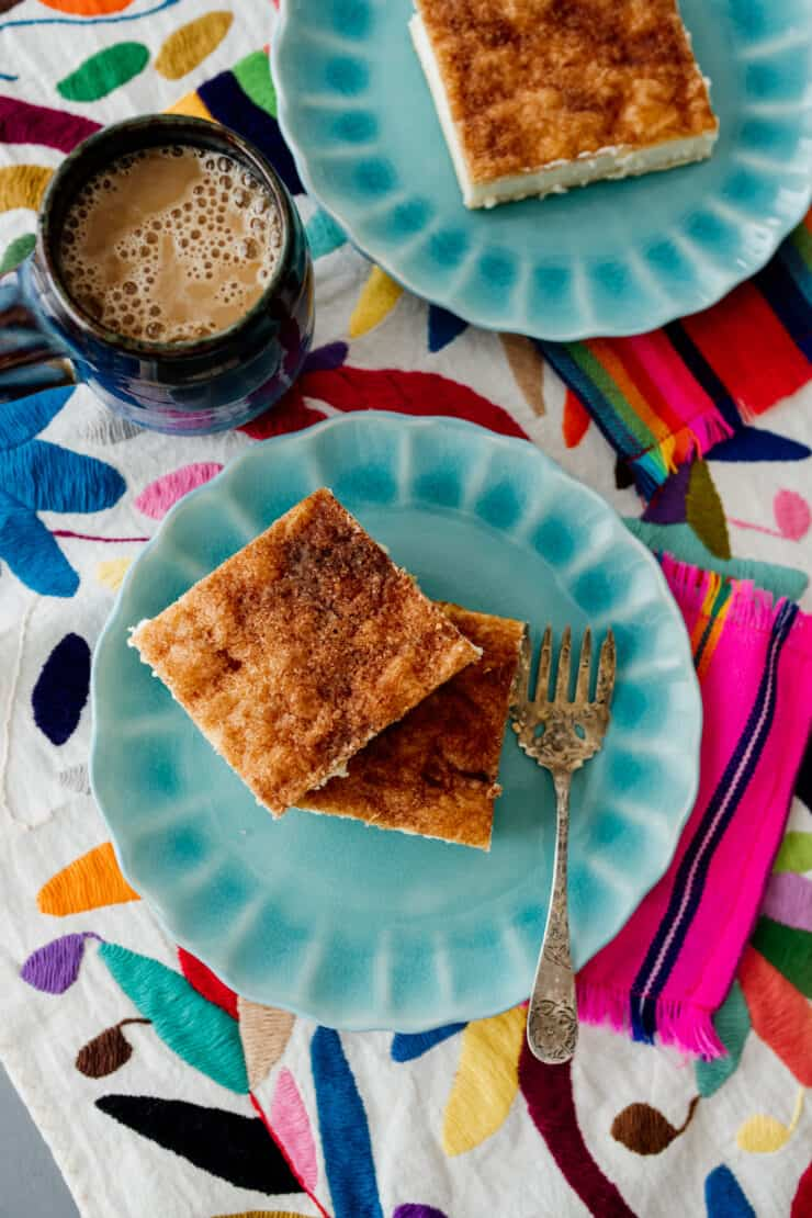 Sopapilla Cheesecake Bars em pratos de marmelada sobre um tecido colorido na mesa com uma xícara de café