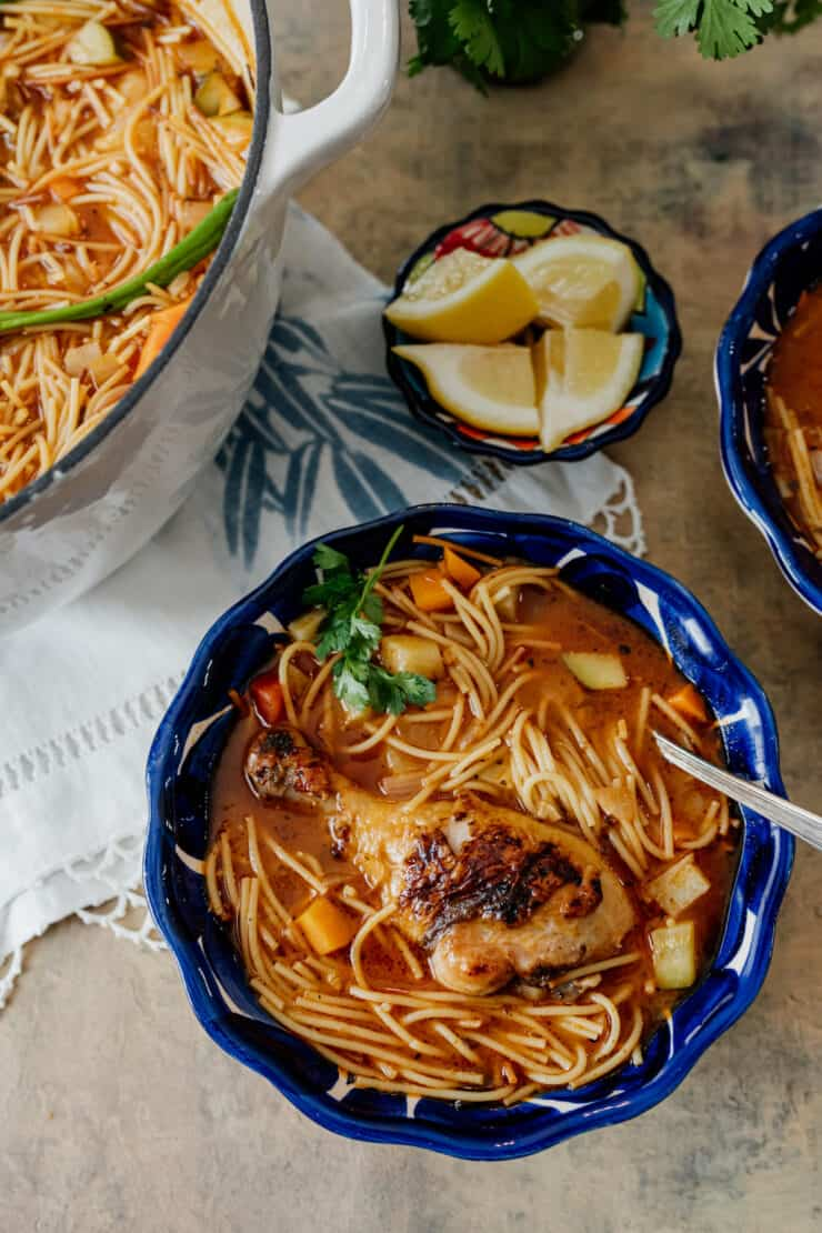 Sopa de Fideos con Pollo, uma versão mexicana de sopa de macarrão de galinha numa tigela azul mexicana com um lado de limões