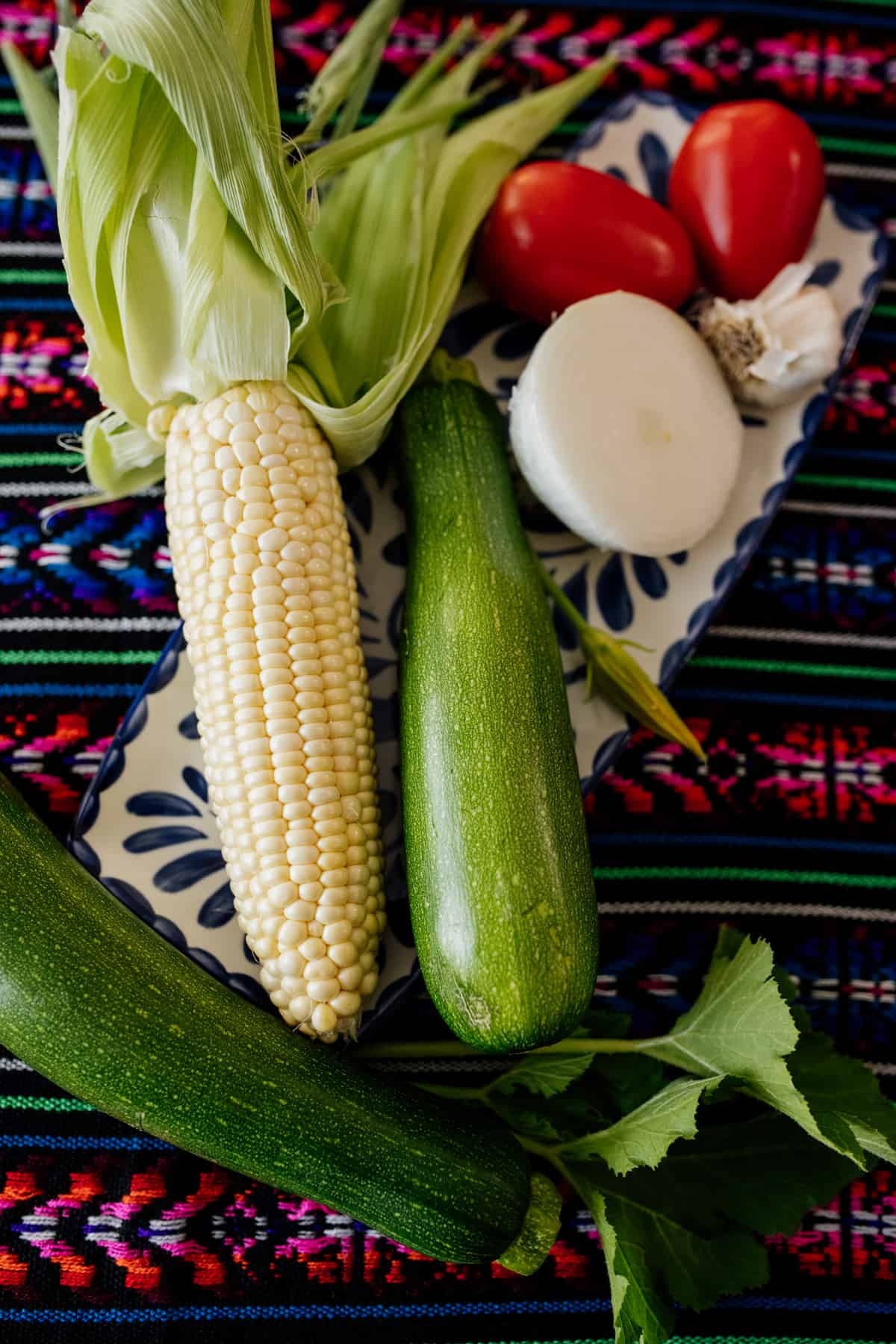 Tomate, cebola, milho e abobrinha em uma pequena bandeja em cima de um colorido corredor mexicano
