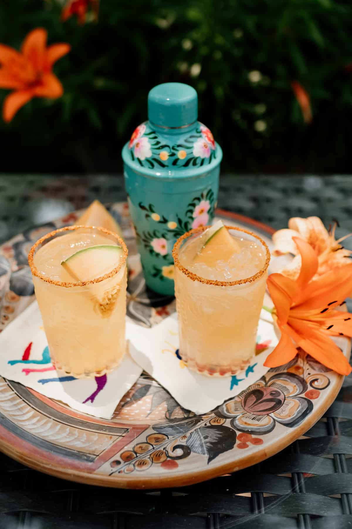 dois copos de Cantaloupe Melon Margaritas com Tajin e Lilly flores na lateral e cocktail shaker no fundo