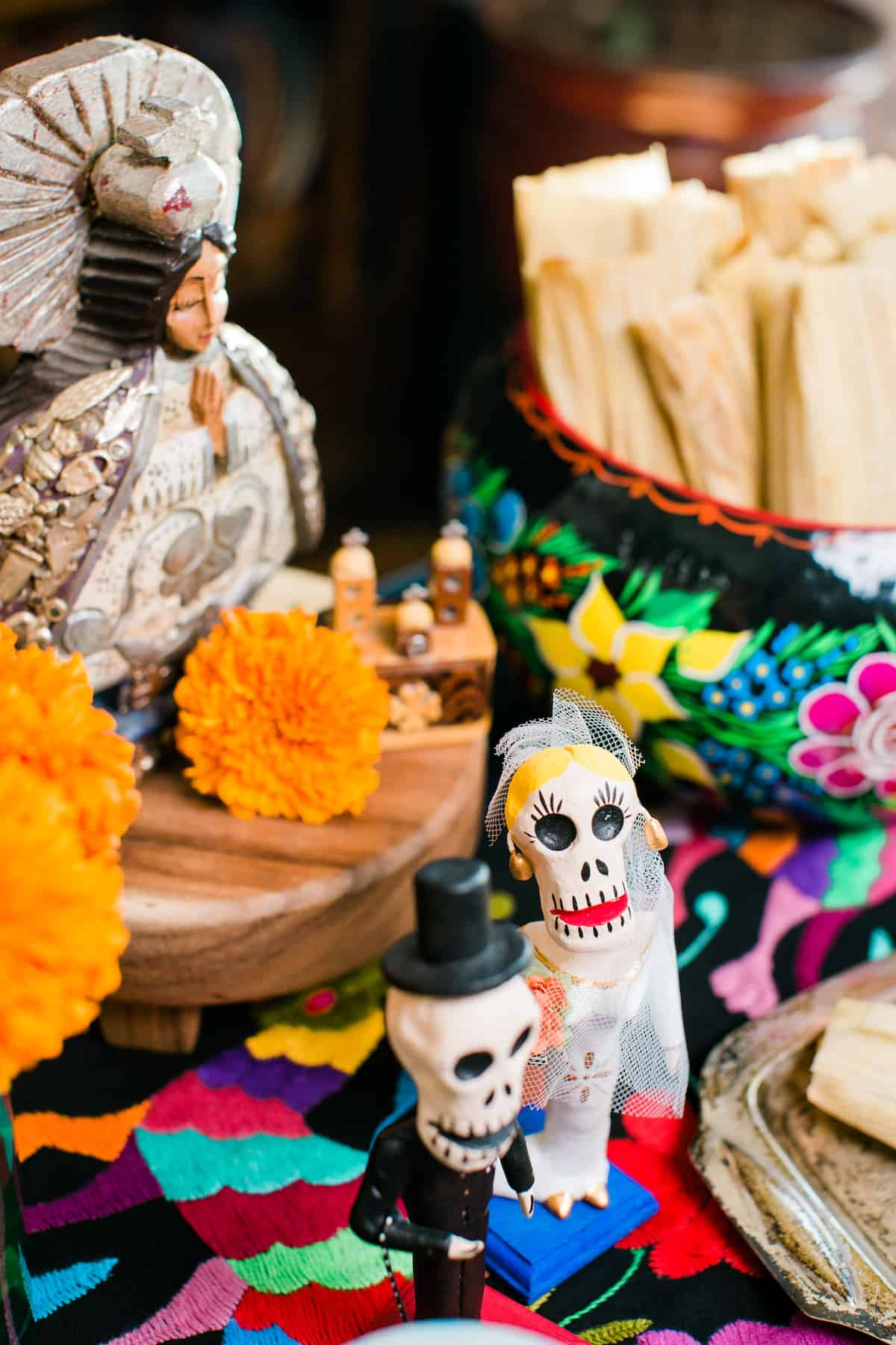 um mini-alterado para Dia de los Muertos adornado com velas, calêndulas, estatuetas e tamales de especiarias de abóbora