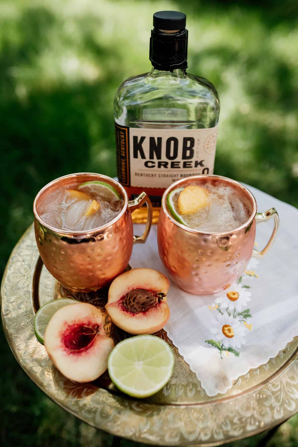 garrafa de "knob creek" junto a dois cocktails de mula de pêssego do kentucky
