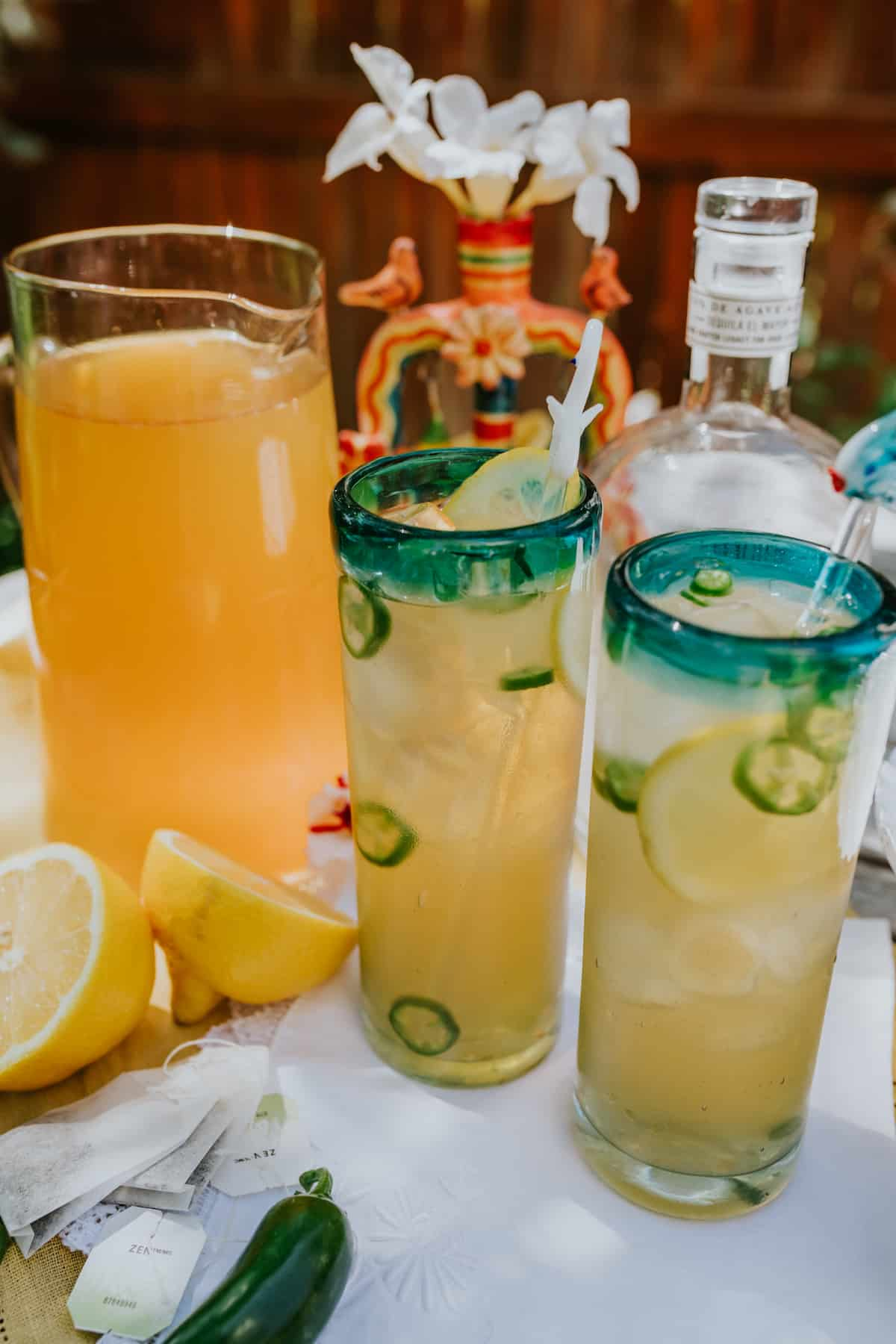 jarra alta de chá verde limonada ao fundo com duas margaritas de palmeira picante em copos verdejantes em primeiro plano