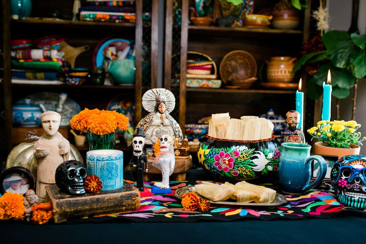 um mini-alterado para Dia de los Muertos adornado com velas, calêndulas, estatuetas e tamales de especiarias de abóbora