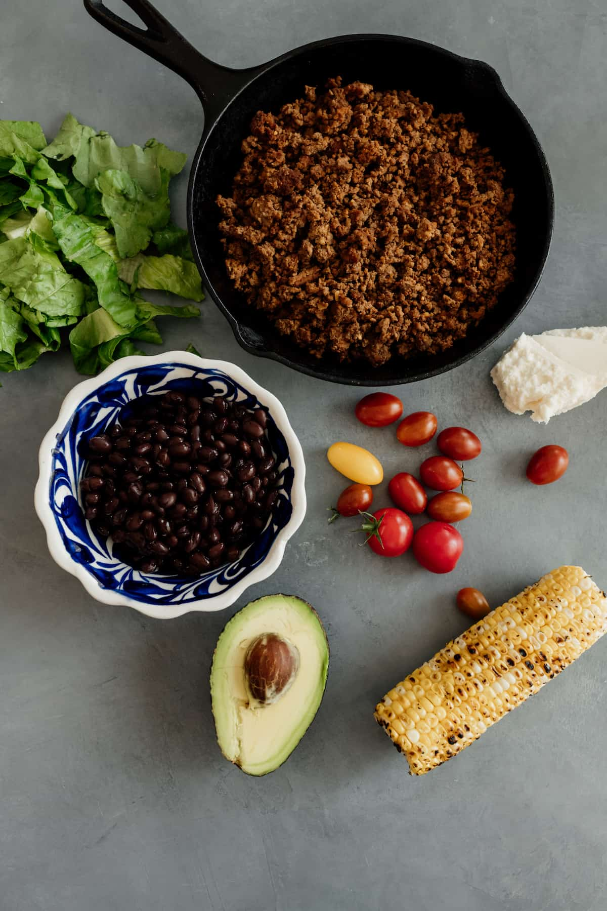 frigideira com bisonte moído e ingredientes para uma salada de tacos - milho, abacate, tomate, feijão preto