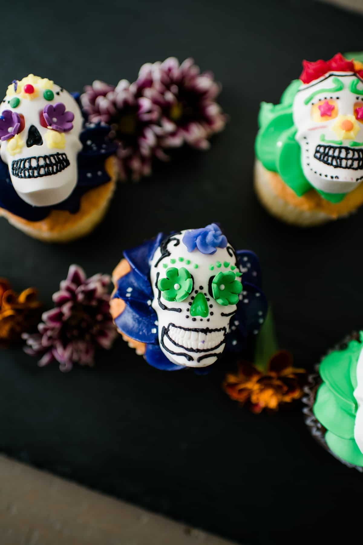 Vista aérea destas caveiras festivas DIY Dia de los Muertos decoradas com cobertura colorida e servidas em cima de um cupcake.