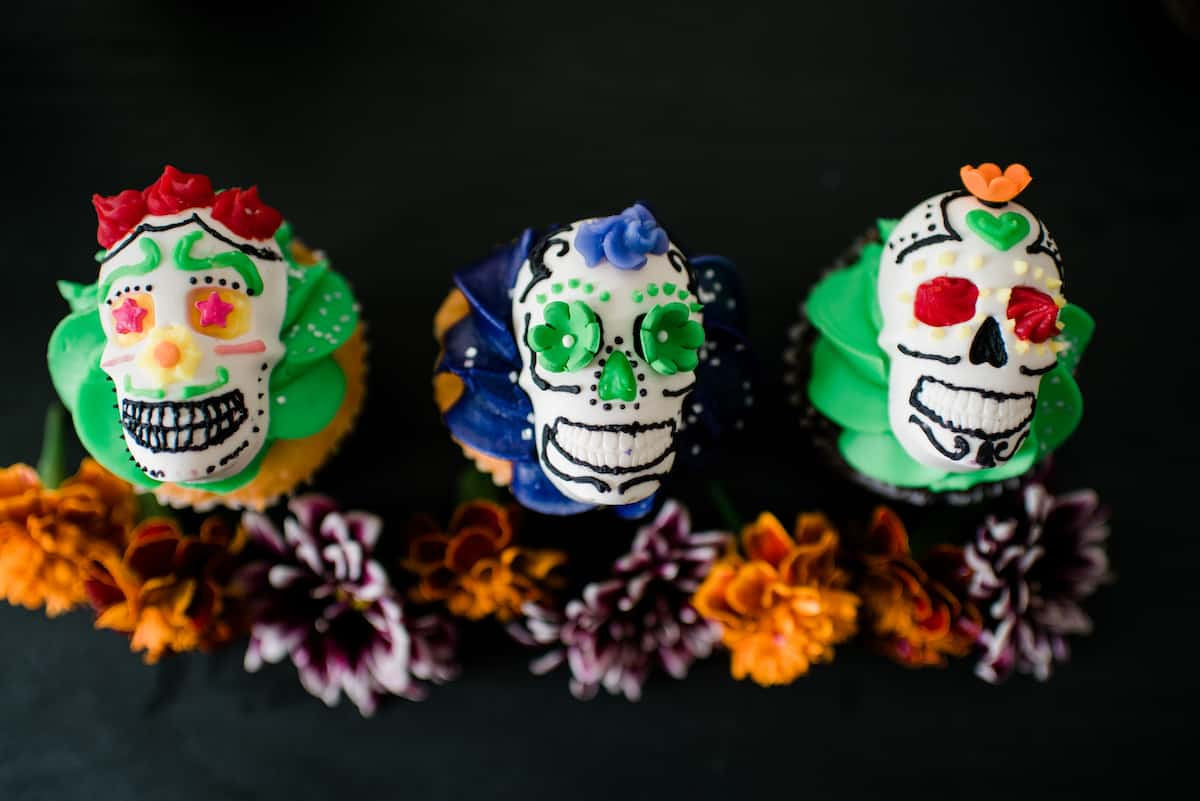 Vista aérea destas caveiras festivas DIY Dia de los Muertos decoradas com cobertura colorida e servidas em cima de um cupcake.