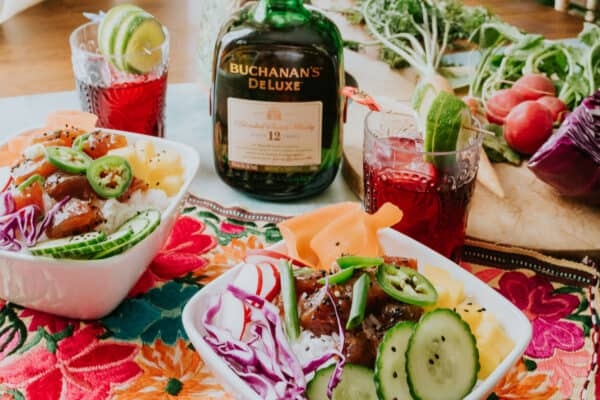 tigelas de atum em uma mesa com whisky hibiscus sours e uma garrafa de buchanan's whisky.
