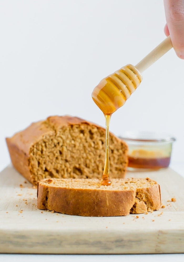Um favo de mel de madeira está chuviscando mel sobre uma fatia de pão integral de mel marrom de trigo. O pão de pão está no fundo.