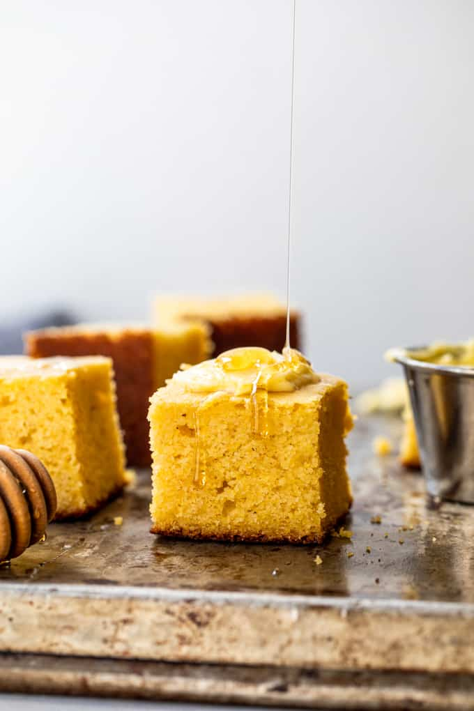 Fatias de pão de milho sendo servidas com manteiga e uma garoa de mel.