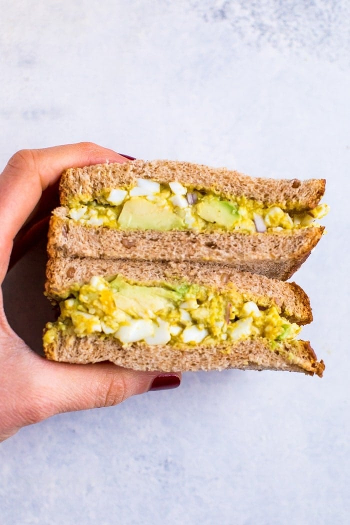 Uma salada de ovo de abacate curado à mão numa sanduíche que é cortada ao meio.