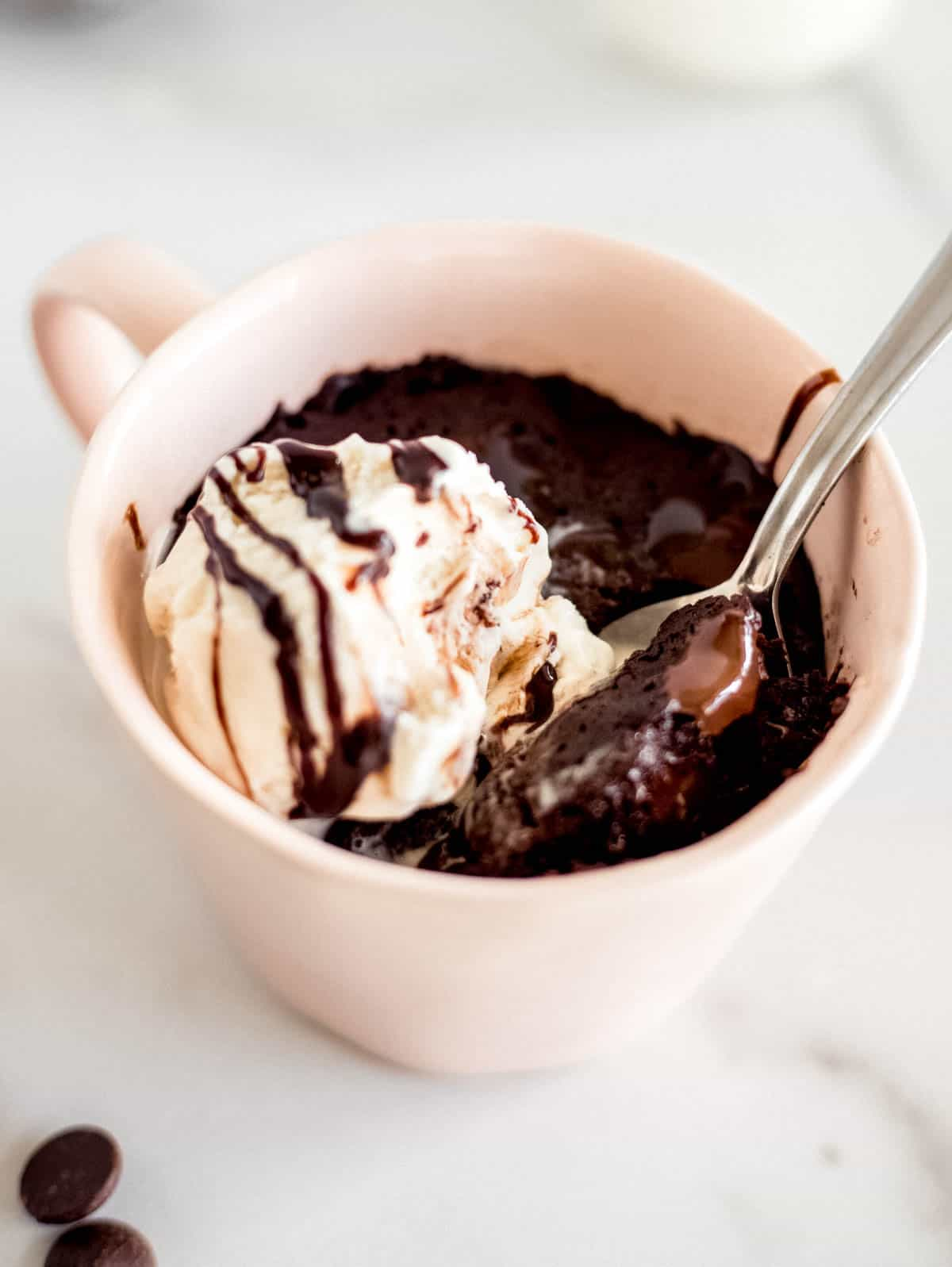 uma colher sentada numa caneca com um brownie de chocolate e uma bola de gelado de baunilha