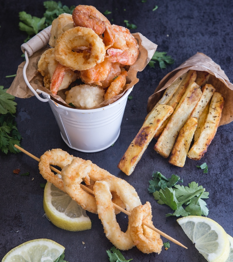 frutos do mar fritos num pequeno balde branco com calamares num pau e batatas fritas num pequeno saco de papel