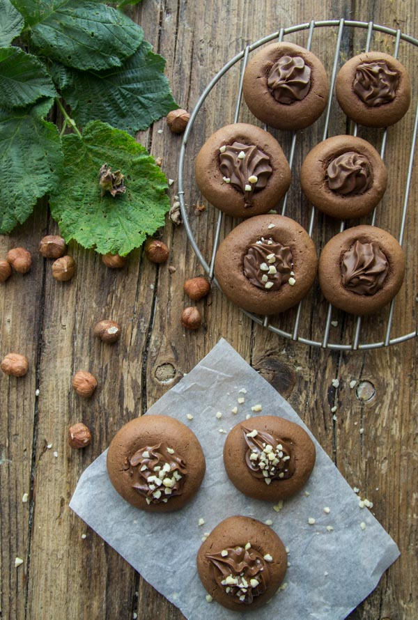 biscoitos redondos cheios de nutella, sobre uma tábua de madeira com avelãs inteiras
