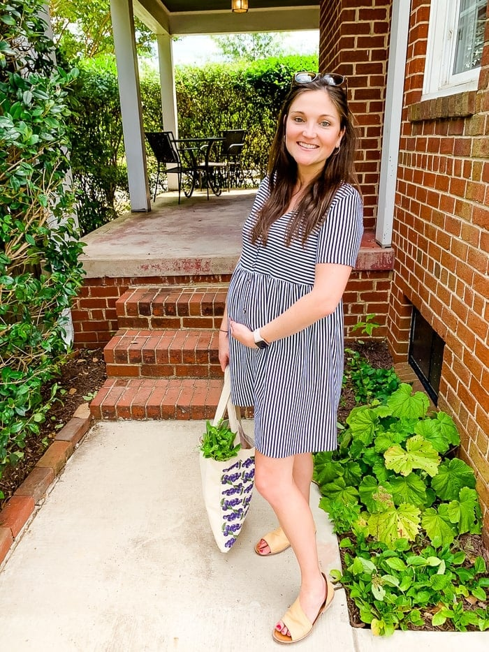 Mulher grávida com um vestido às riscas a sorrir lá fora com um saco de legumes.