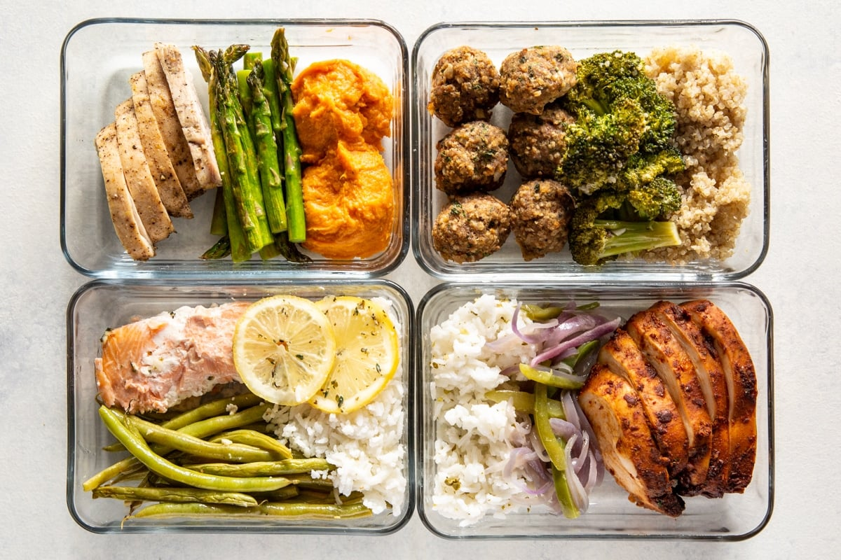 4 recipientes de vidro cheios com alimentos preparados para refeições como vegetais, arroz, frango e salmão.