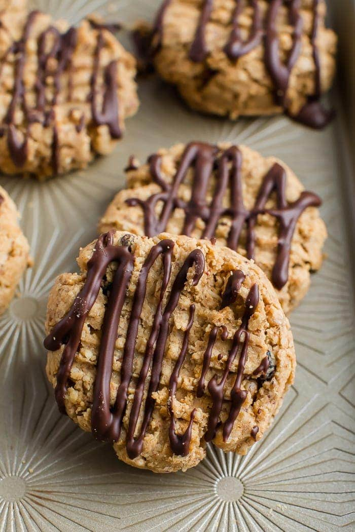 Quatro biscoitos de granola de manteiga de amendoim, regados com chocolate, sentados em uma bandeja de cor neutra.