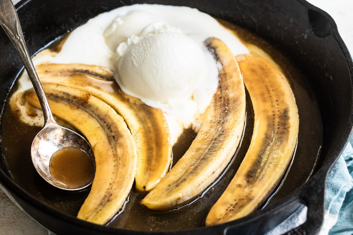 Bananas foster em uma frigideira preta com uma colher de servir repousando nela.
