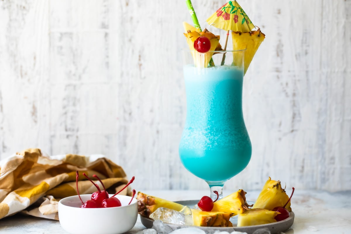 Um cocktail havaiano azul rodeado de ananás e cerejas marasquino.
