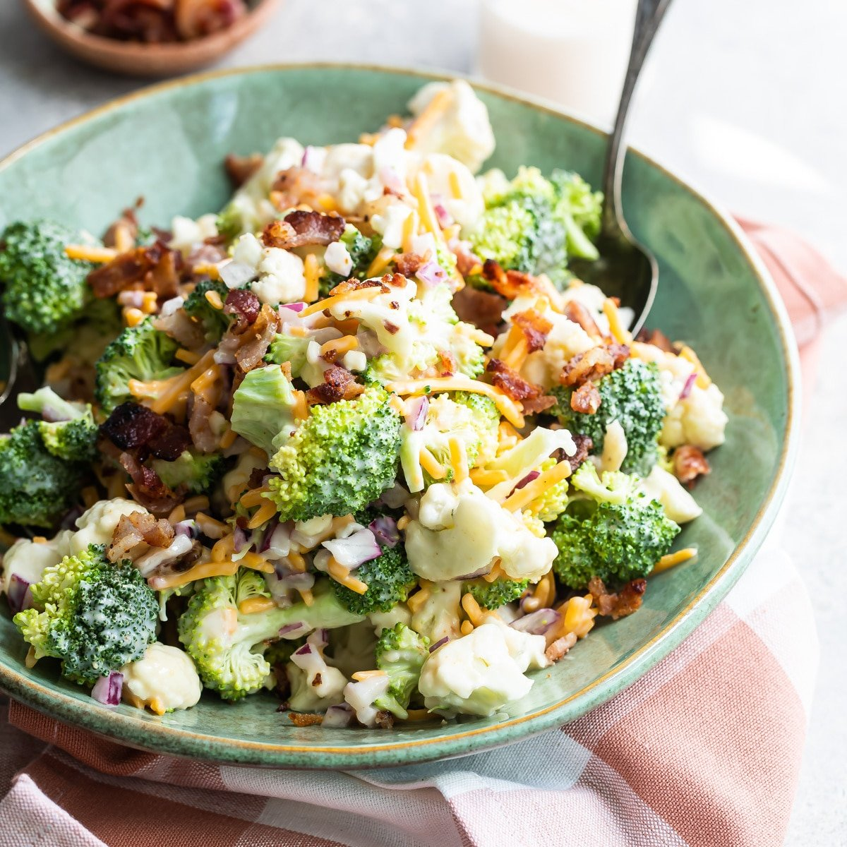 Salada de brócolos com bacon e queijo numa tigela verde com uma colher.