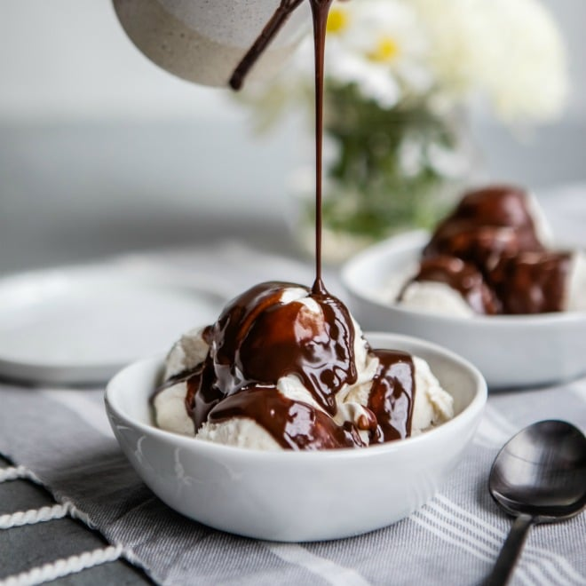 Molho de chocolate a ser regado com gelado de baunilha numa tigela branca.