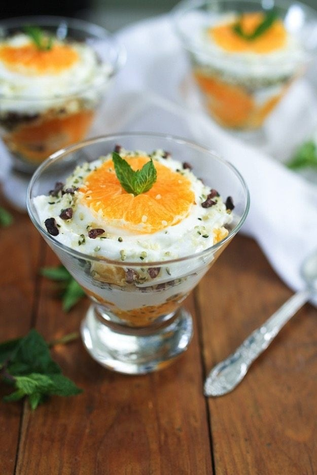 Tigela de vidro de parfait de iogurte grego clementina com duas outras tigelas ao fundo.