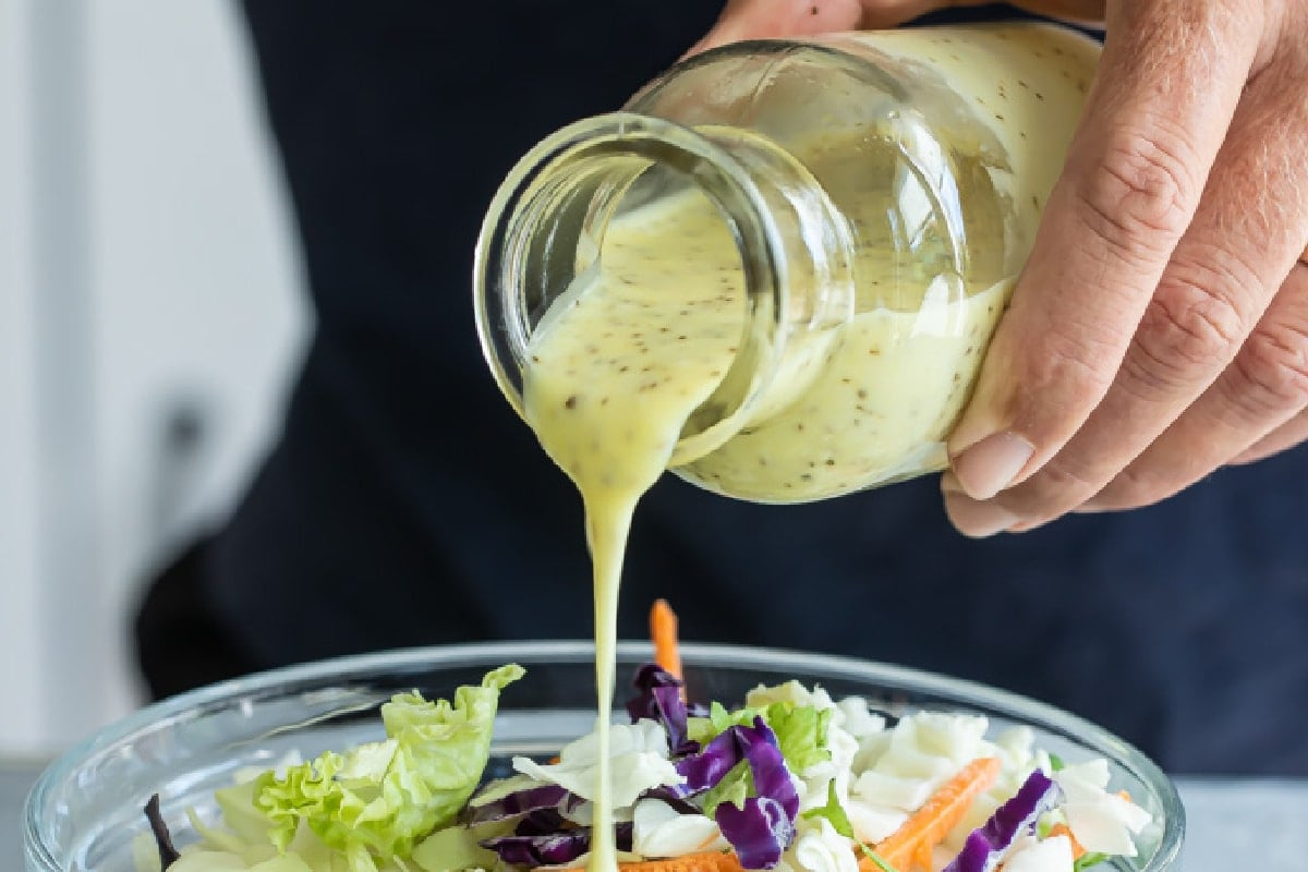 Molho de salada de repolho a ser deitado numa grande tigela de repolho transparente.