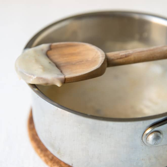 Creme condensado de sopa de galinha sobre uma colher de pau, descansando num pote de prata.