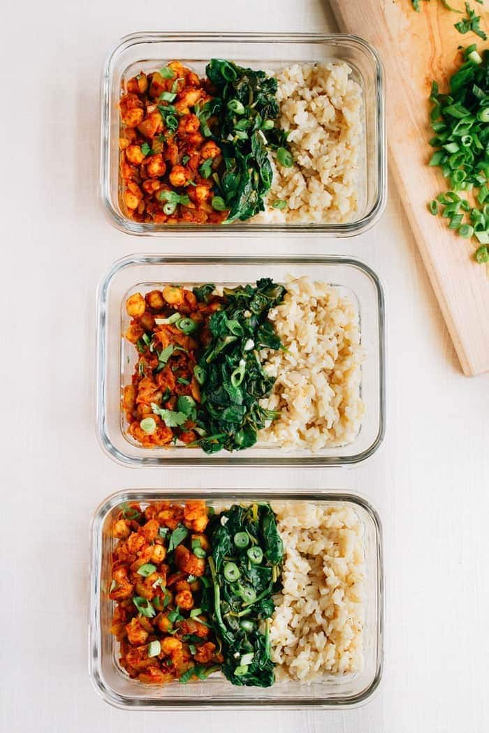 Três recipientes de vidro, cada um com filas de grão de bico frito, espinafres salteados com alho e arroz branco.