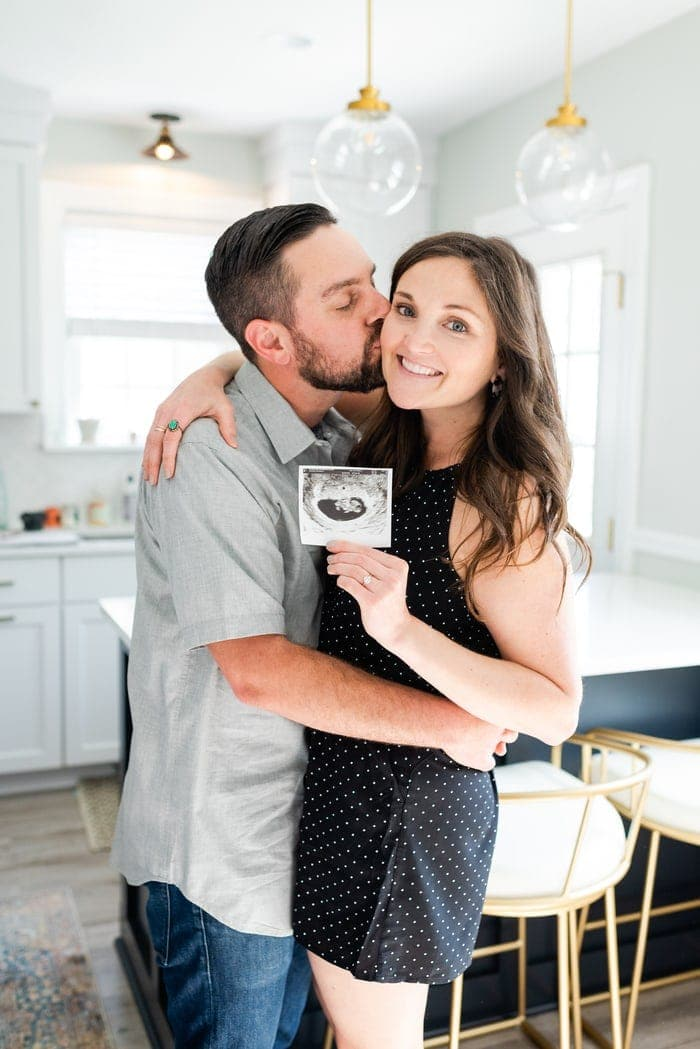 Homem a beijar mulher na bochecha. Mulher segurando uma foto de sonograma e sorrindo.