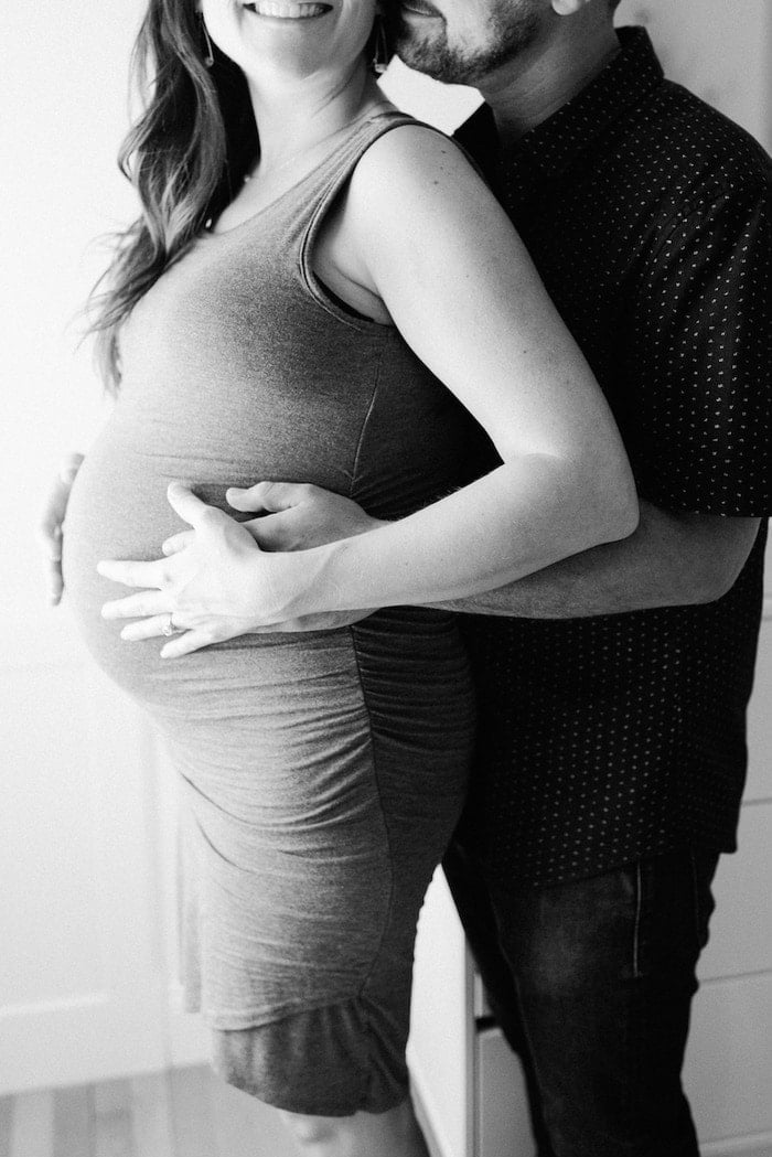 Casal heterossexual abraçando para um retrato de maternidade em preto e branco.