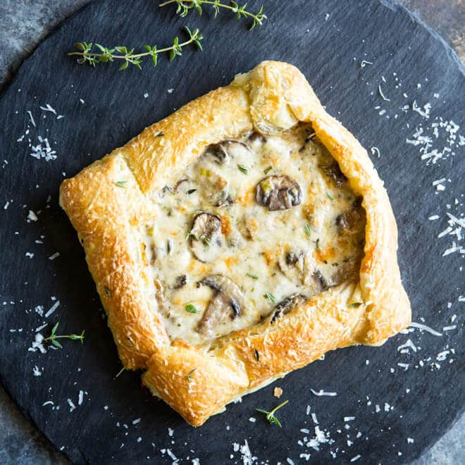 Uma tarte de cogumelos e alho francês coberta com tomilho verde fresco e queijo parmesão recém ralado num prato preto.