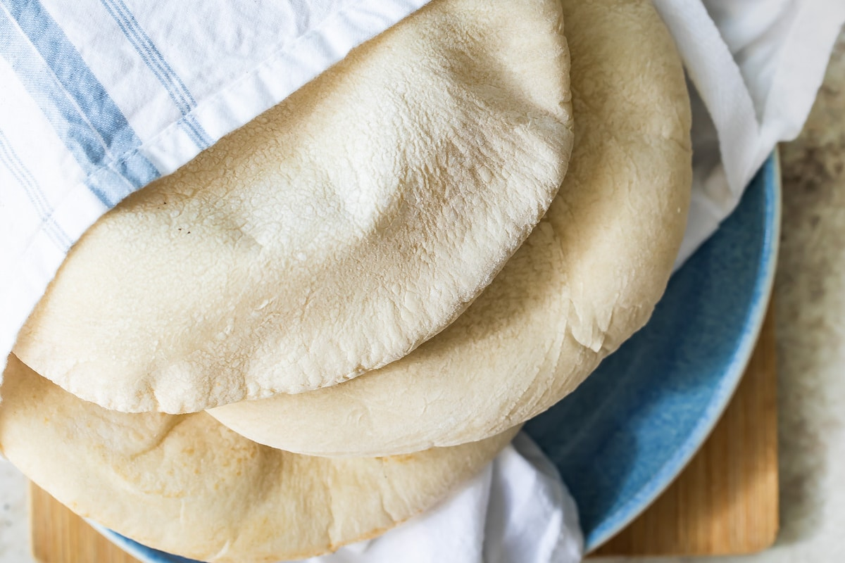 Três pedaços de pão pita caseiro envoltos numa toalha de linho num prato azul.