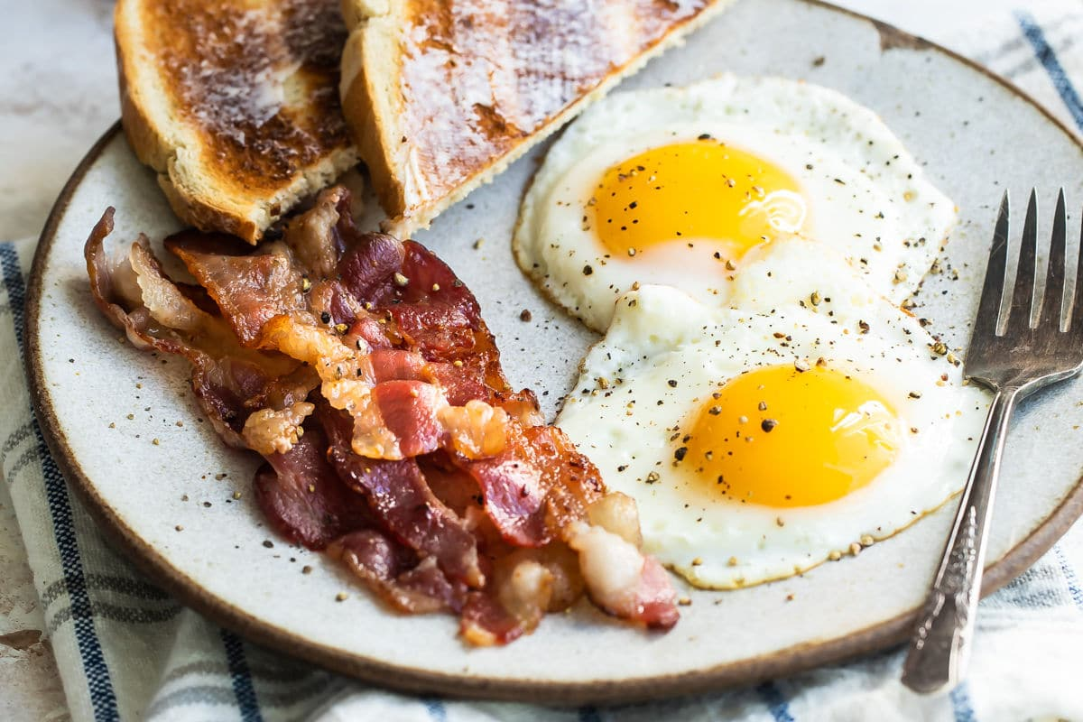 Ovos ensolarados em um prato com bacon e torradas.