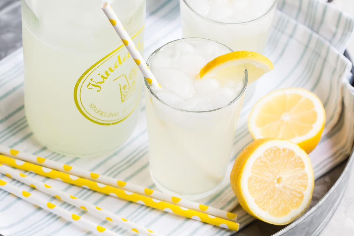 Limonada em copos numa bandeja de prata com palhinhas amarelas e brancas e guarnição de limão.